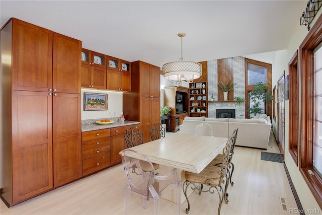 kitchen with glass insert cabinets, decorative light fixtures, a fireplace, and light wood-style flooring