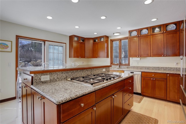 kitchen with light stone counters, glass insert cabinets, stainless steel appliances, a sink, and recessed lighting