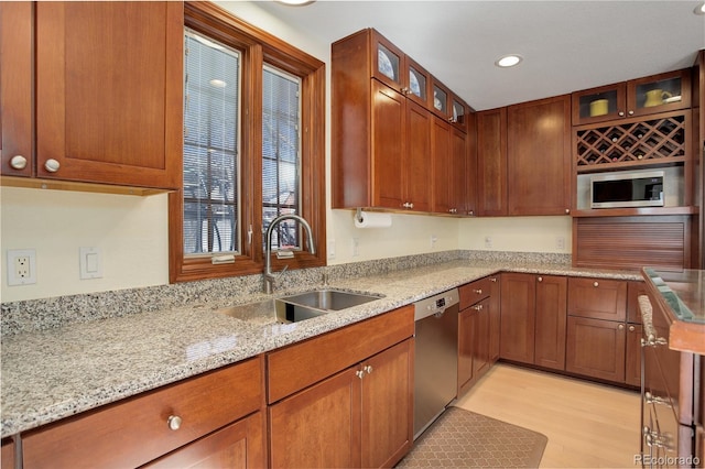 kitchen with glass insert cabinets, light stone counters, stainless steel appliances, light wood-type flooring, and a sink