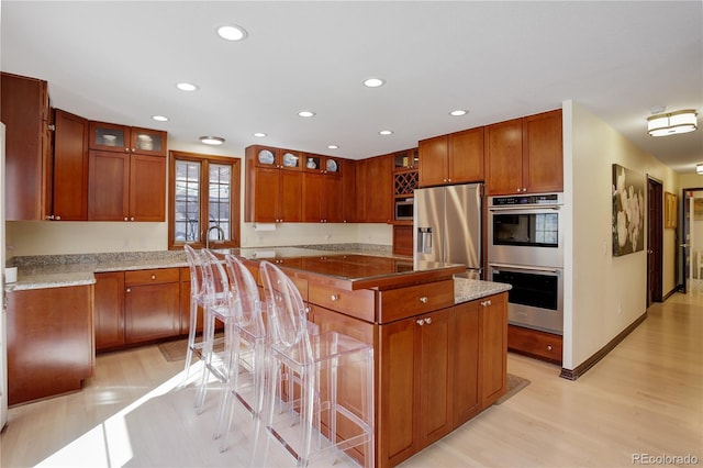 kitchen featuring brown cabinetry, glass insert cabinets, stainless steel appliances, and a center island