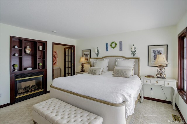 bedroom with baseboards, light colored carpet, and a glass covered fireplace