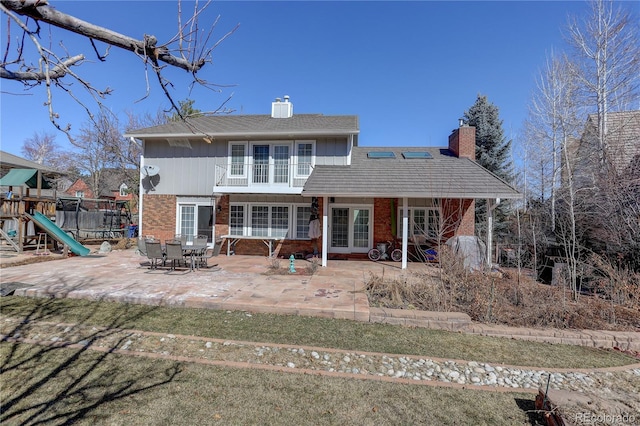 back of house with a playground, brick siding, french doors, a chimney, and a patio area