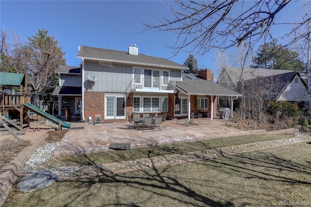 rear view of house with a playground, brick siding, a chimney, board and batten siding, and a patio area