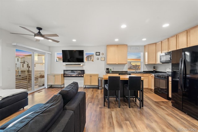 kitchen with light brown cabinetry, open floor plan, black appliances, and light wood-type flooring