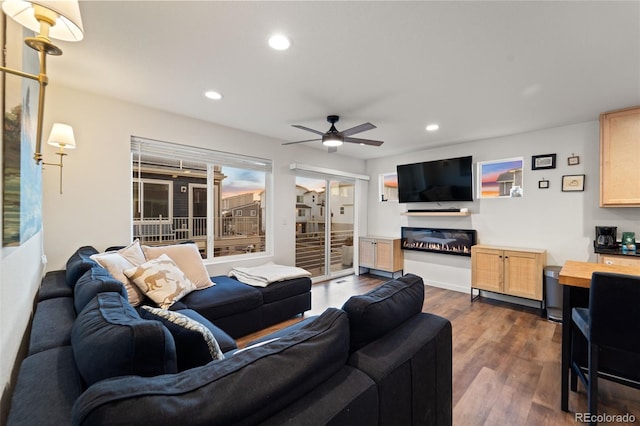 living room featuring dark wood finished floors, a glass covered fireplace, recessed lighting, and ceiling fan