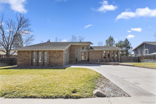 view of front facade with fence, a chimney, concrete driveway, a front lawn, and brick siding