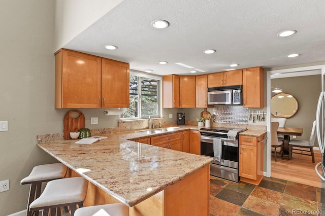 kitchen featuring a sink, light stone counters, a kitchen breakfast bar, appliances with stainless steel finishes, and a peninsula