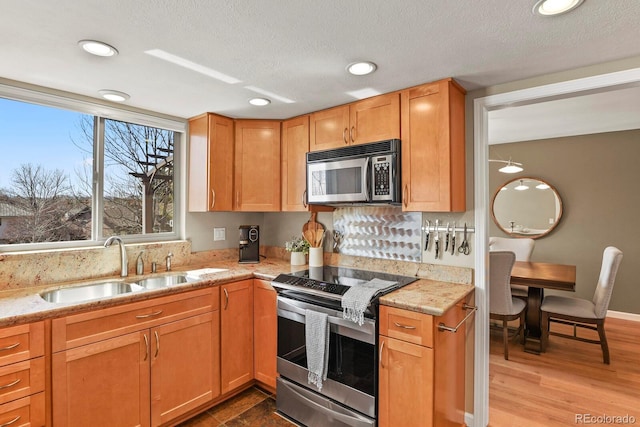 kitchen with a sink, light stone countertops, light wood-style floors, and appliances with stainless steel finishes