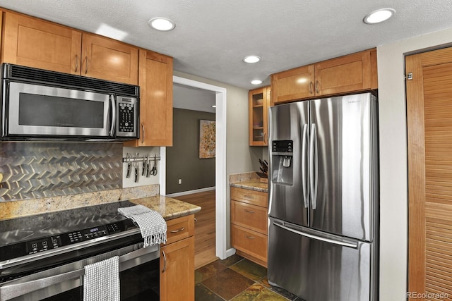 kitchen with light stone counters, stainless steel appliances, brown cabinets, and a textured ceiling