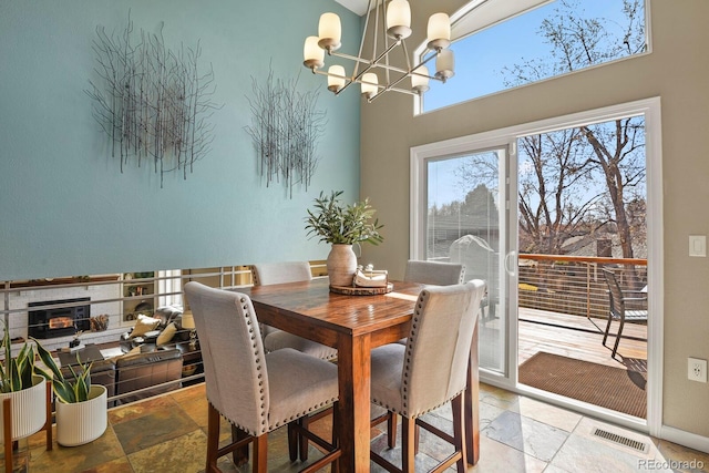 dining room featuring visible vents, stone tile floors, a towering ceiling, baseboards, and a chandelier