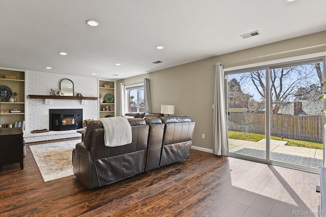 living area featuring dark wood-type flooring, a brick fireplace, plenty of natural light, and visible vents