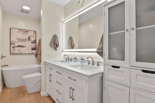 bathroom with double vanity, a freestanding tub, wood finished floors, and a sink