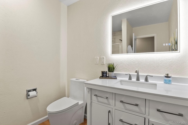 bathroom featuring baseboards, toilet, vanity, and a textured wall