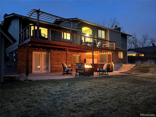 rear view of house with brick siding, an outdoor fire pit, a lawn, a chimney, and a patio