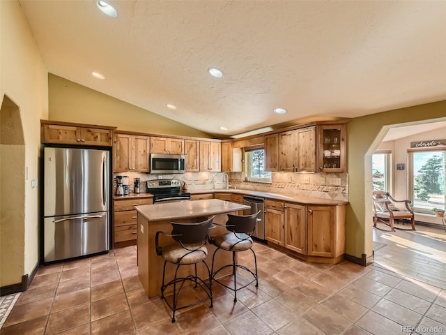 kitchen featuring a healthy amount of sunlight, vaulted ceiling, stainless steel appliances, and decorative backsplash