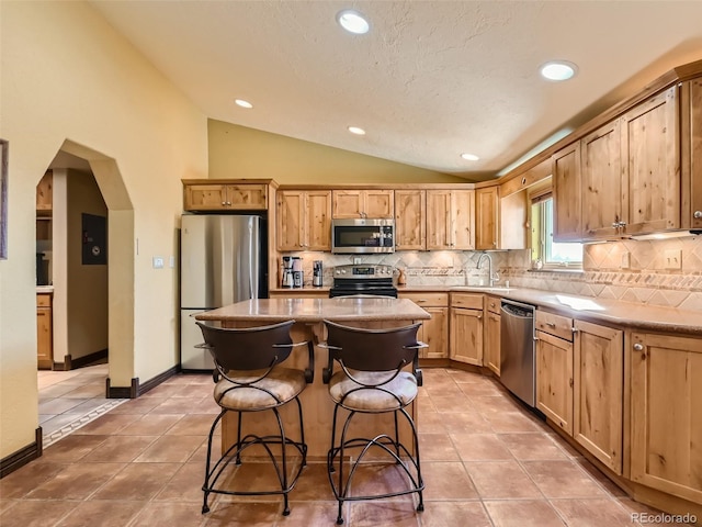 kitchen with arched walkways, a kitchen island, vaulted ceiling, appliances with stainless steel finishes, and decorative backsplash