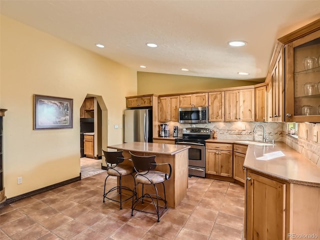 kitchen featuring arched walkways, decorative backsplash, vaulted ceiling, stainless steel appliances, and a sink