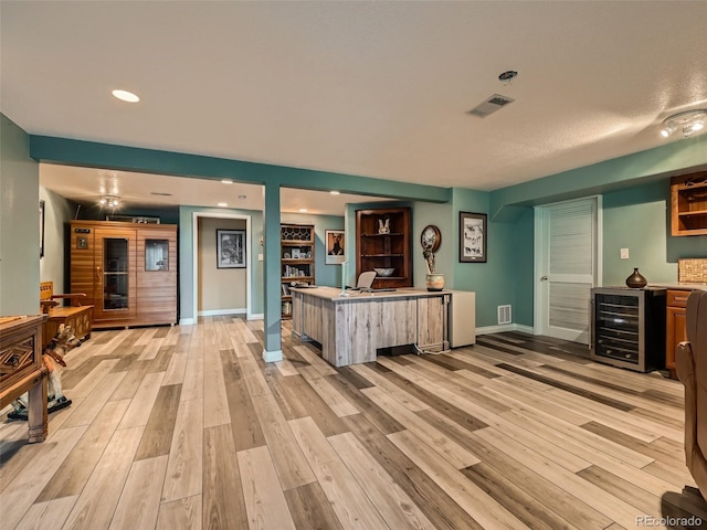 interior space with beverage cooler, light wood finished floors, visible vents, and baseboards