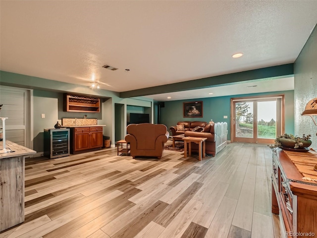 living room featuring wine cooler, indoor wet bar, visible vents, and light wood finished floors