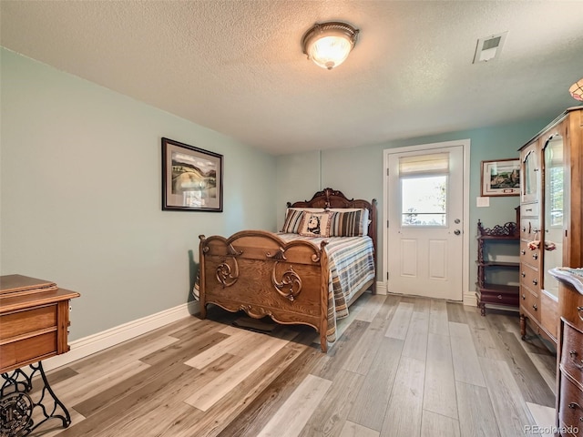 bedroom featuring visible vents, baseboards, a textured ceiling, and light wood finished floors