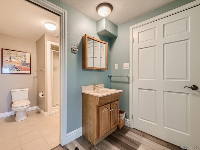 bathroom featuring a textured ceiling, toilet, wood finished floors, vanity, and baseboards