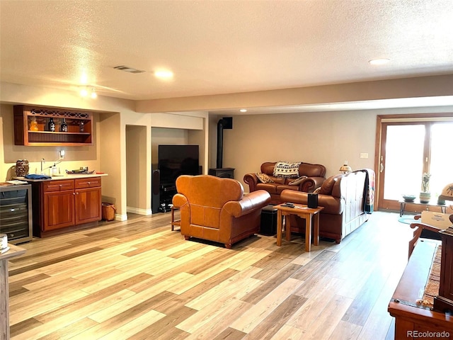 living room featuring visible vents, light wood-style flooring, wine cooler, a wood stove, and wet bar