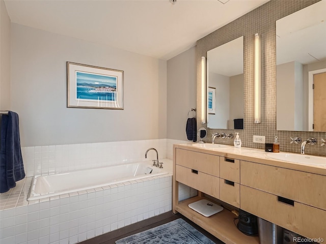 bathroom featuring tile walls, large vanity, dual sinks, tiled tub, and tasteful backsplash