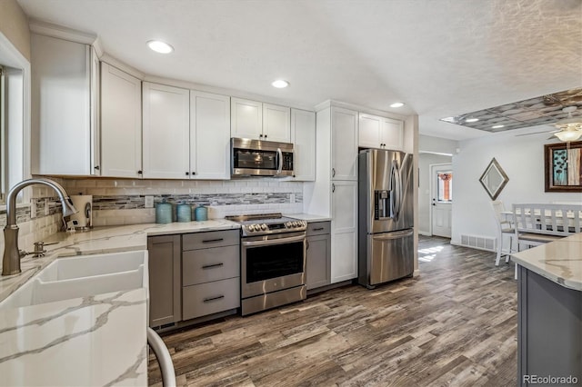 kitchen featuring stainless steel appliances, light stone countertops, white cabinets, dark hardwood / wood-style flooring, and decorative backsplash