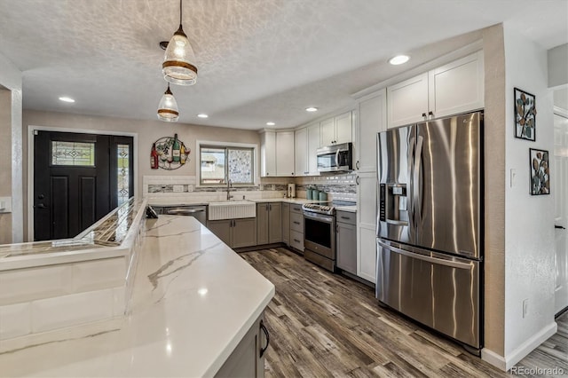 kitchen featuring decorative light fixtures, sink, white cabinets, stainless steel appliances, and light stone countertops