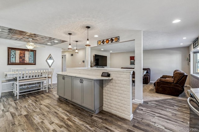 kitchen with gray cabinets, a kitchen island, dark hardwood / wood-style floors, decorative light fixtures, and light stone countertops