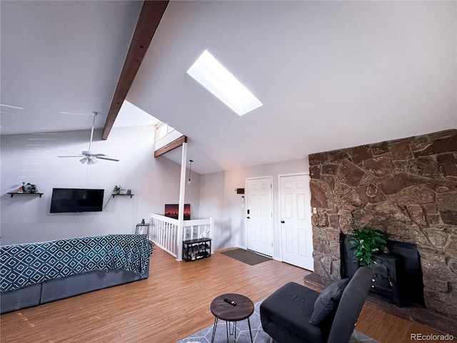 living area featuring a wood stove, lofted ceiling with skylight, wood finished floors, and a ceiling fan