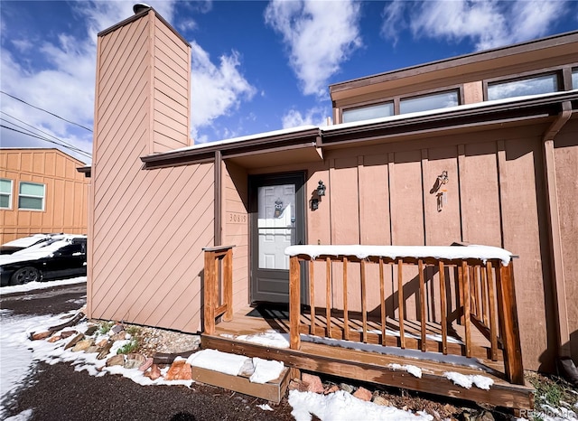 snow covered property entrance with board and batten siding and a chimney