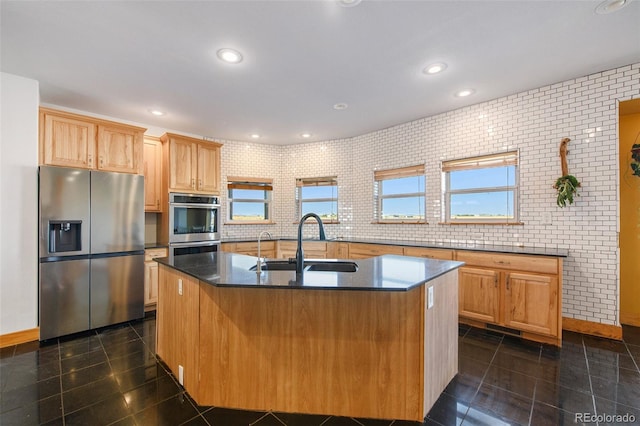 kitchen with stainless steel appliances, sink, light brown cabinets, an island with sink, and decorative backsplash