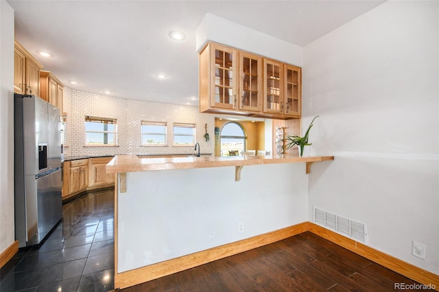 kitchen featuring stainless steel fridge with ice dispenser, dark wood-type flooring, kitchen peninsula, and a breakfast bar area