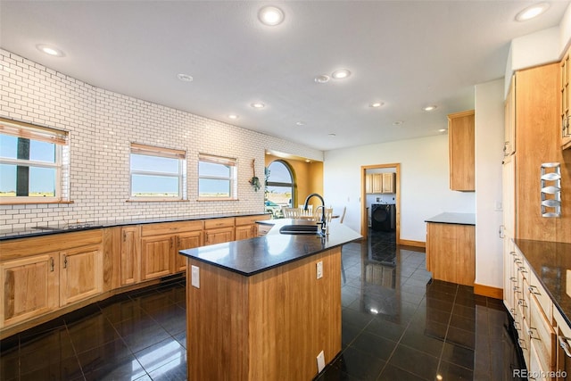 kitchen featuring dark tile patterned flooring, backsplash, an island with sink, and sink