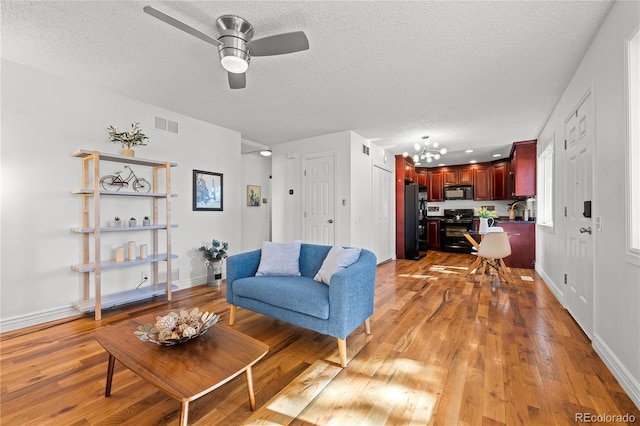 living area featuring a textured ceiling, baseboards, visible vents, and light wood-style floors