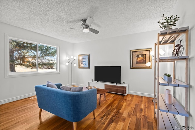 living area with ceiling fan, a textured ceiling, baseboards, and wood finished floors