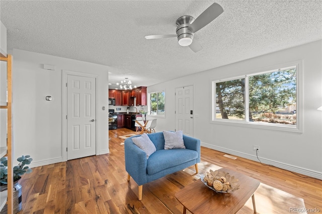 living area featuring light wood-style floors, a textured ceiling, baseboards, and a ceiling fan