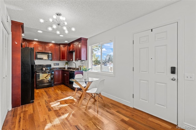 kitchen with light wood-style floors, dark countertops, dark brown cabinets, black appliances, and a chandelier