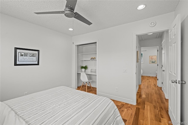 bedroom featuring attic access, baseboards, light wood-style flooring, a textured ceiling, and a closet