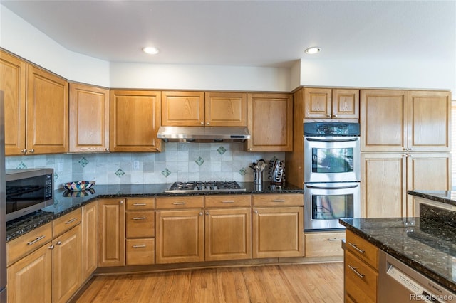 14261 W Evans Cir, Lakewood, CO 80228 - kitchen featuring stainless steel appliances, under cabinet range hood, dark stone countertops, brown cabinetry, and recessed lighting