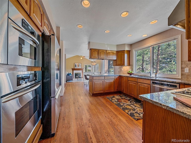 4228 Scenic Village Dr, Evergreen, CO 80439 - kitchen with stainless steel appliances, a peninsula, brown cabinetry, recessed lighting, and light wood-style flooring