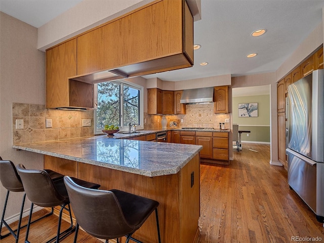 4228 Scenic Village Dr, Evergreen, CO 80439 - kitchen featuring stainless steel appliances, a peninsula, brown cabinetry, wall chimney exhaust hood, and a kitchen bar