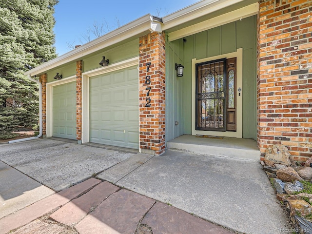doorway to property featuring driveway, brick siding, an attached garage, and board and batten siding