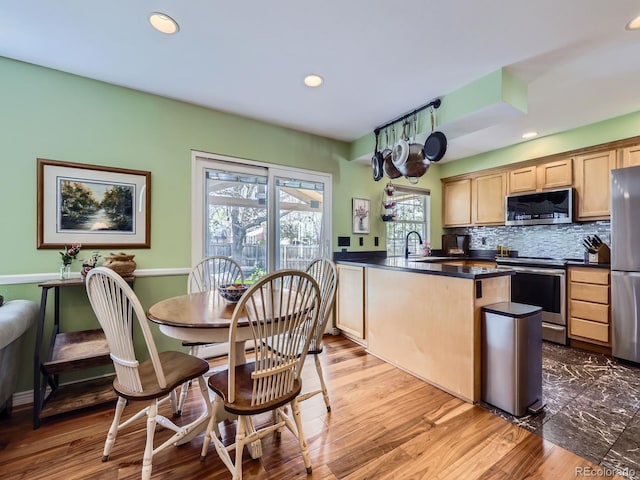 kitchen featuring appliances with stainless steel finishes, dark countertops, a peninsula, recessed lighting, and backsplash
