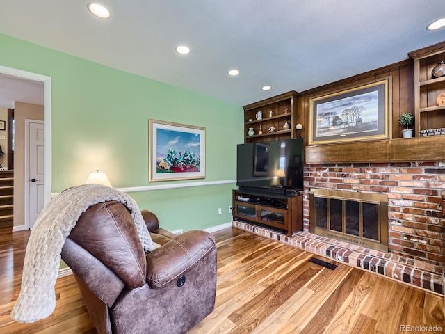 living area featuring recessed lighting, wood finished floors, baseboards, and a brick fireplace