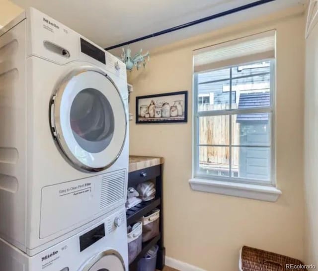 laundry area with estacked washer and dryer and baseboards
