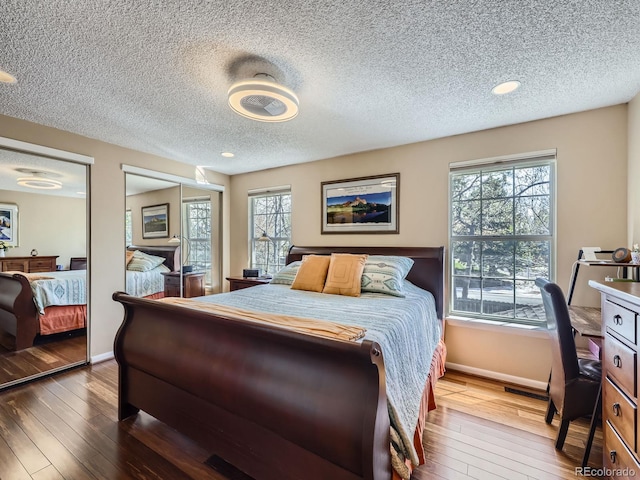 bedroom with baseboards, a textured ceiling, wood-type flooring, multiple windows, and multiple closets