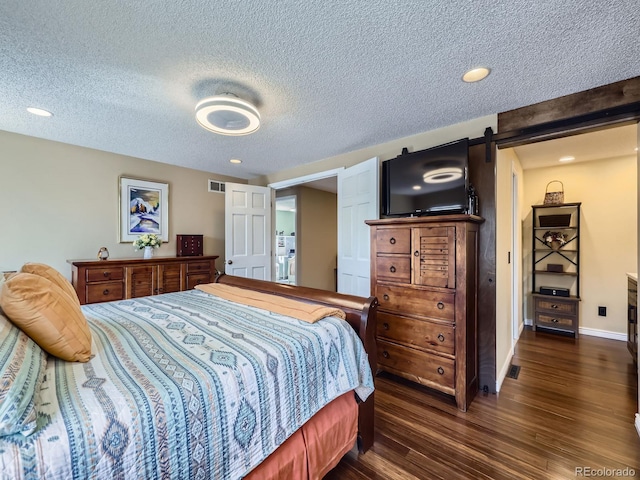 bedroom featuring a barn door, dark wood-type flooring, a textured ceiling, and recessed lighting