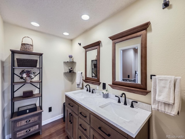 full bathroom with wood finished floors, double vanity, a textured ceiling, recessed lighting, and baseboards